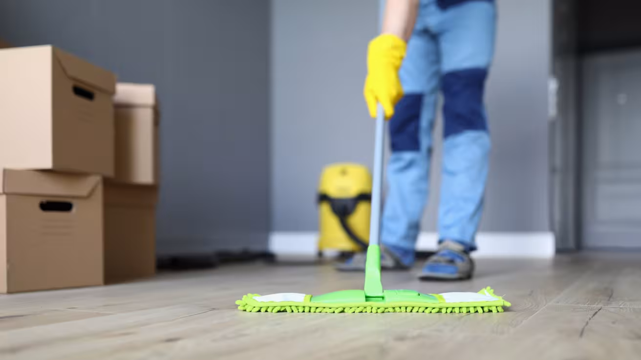 Person wischt mit gr&uuml;nem Wischmopp und gelben Handschuhen hellen Boden.